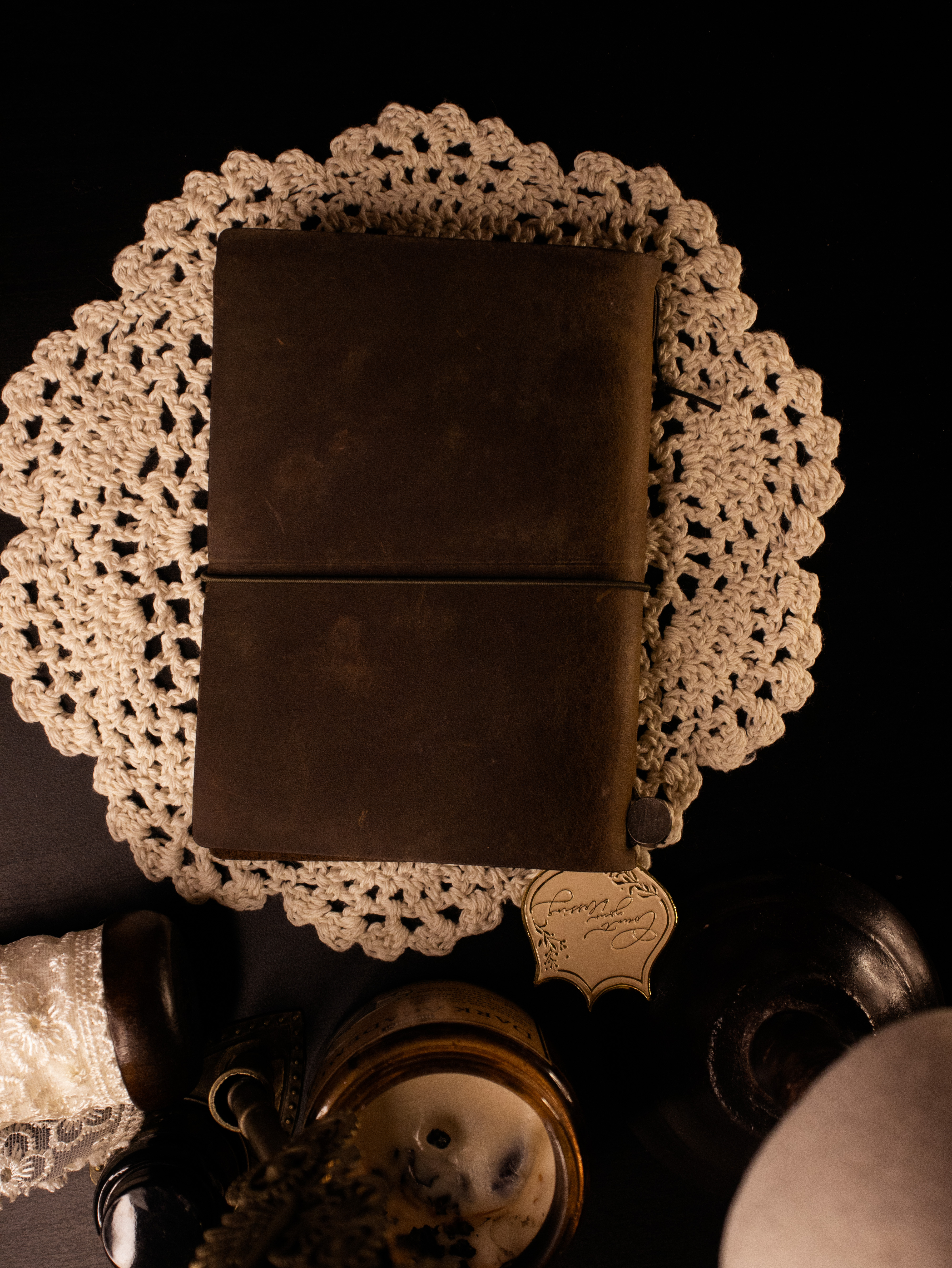 A worn leather journal resting on a crocheted doily beside vintage objects