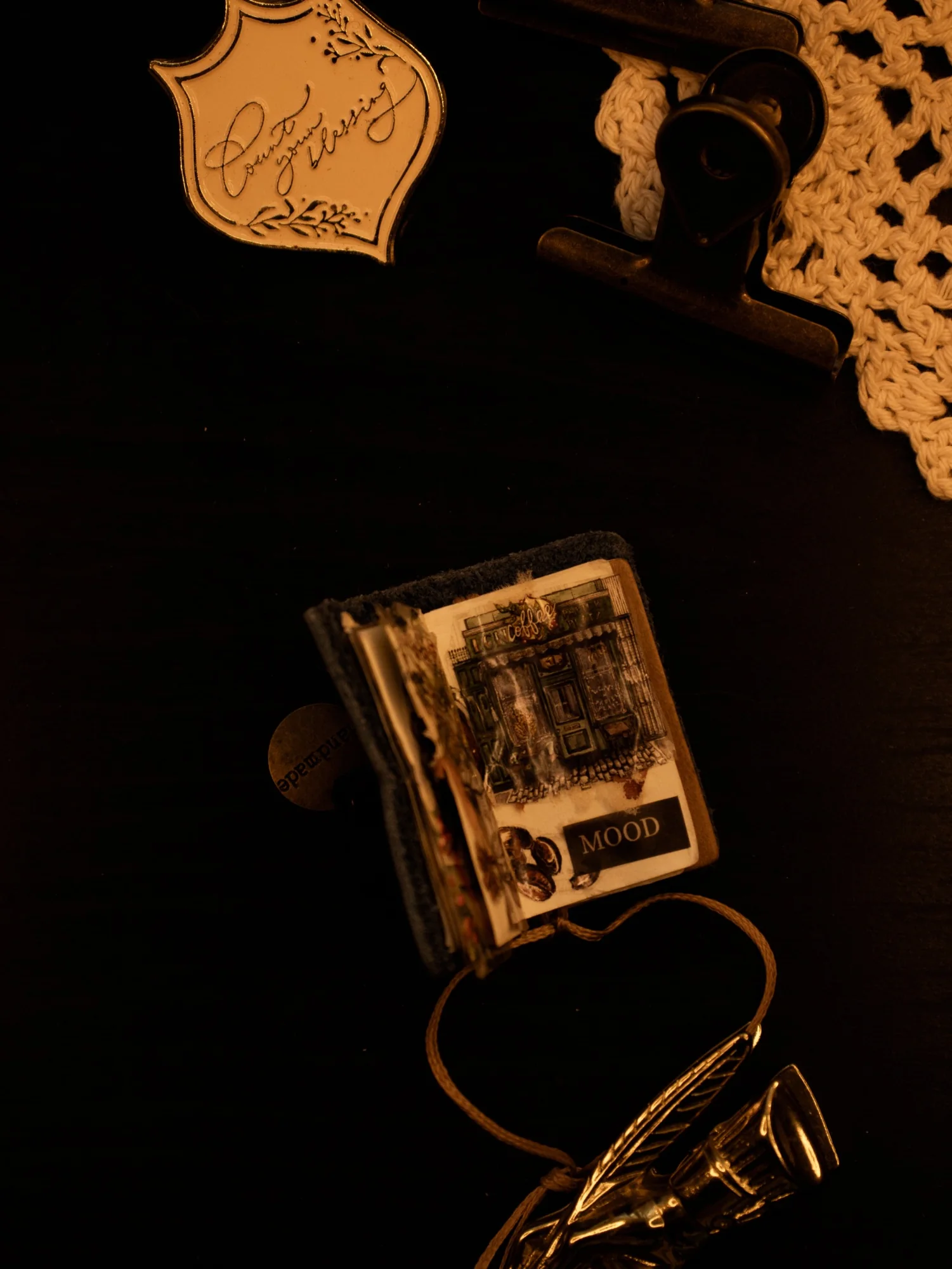 A small decorated journal tucked into a dark tabletop still life with vintage desk objects